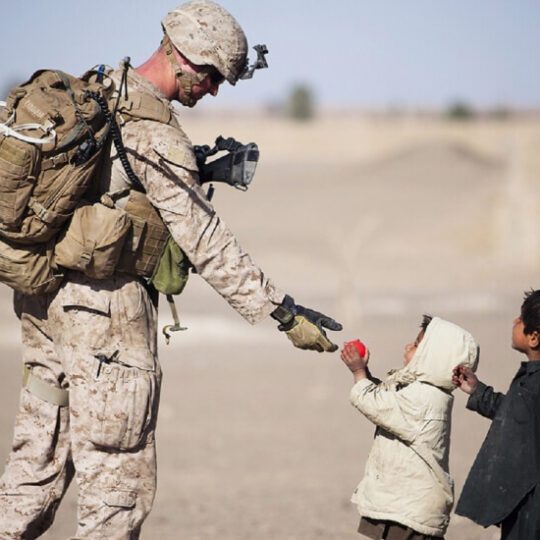 Soldier giving toys to two young children.
